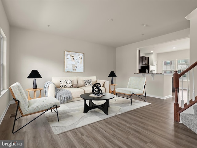 living room featuring wood finished floors, visible vents, baseboards, and stairs