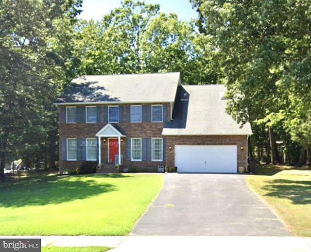 colonial home with aphalt driveway, a garage, brick siding, and a front lawn