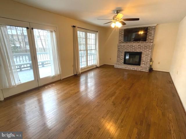 unfurnished living room with a brick fireplace, ceiling fan, and wood finished floors