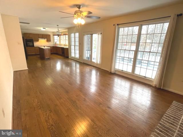 unfurnished living room featuring ceiling fan, baseboards, and dark wood-type flooring