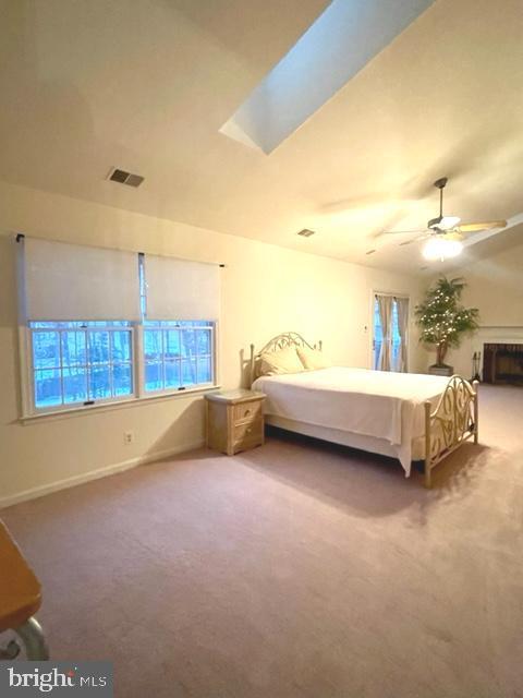 carpeted bedroom with a skylight, baseboards, visible vents, and a ceiling fan