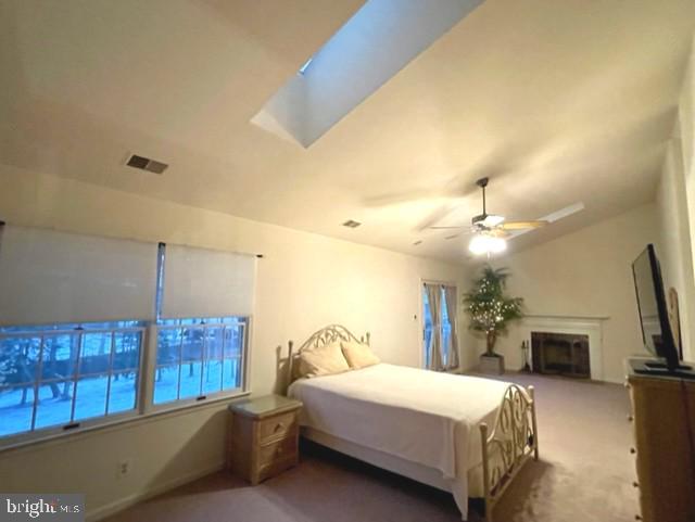 bedroom with carpet, vaulted ceiling with skylight, a fireplace, and multiple windows