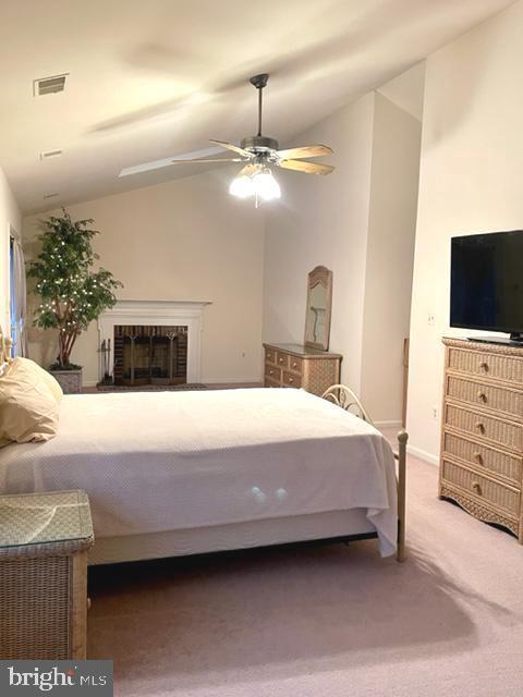 carpeted bedroom with a fireplace, visible vents, vaulted ceiling, and a ceiling fan