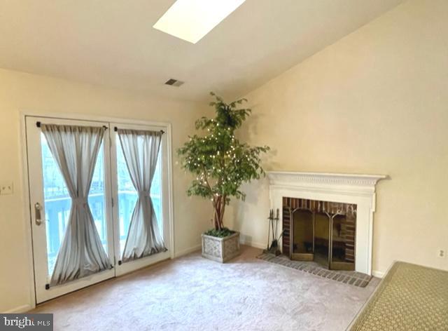 unfurnished living room with baseboards, visible vents, lofted ceiling with skylight, carpet flooring, and a fireplace