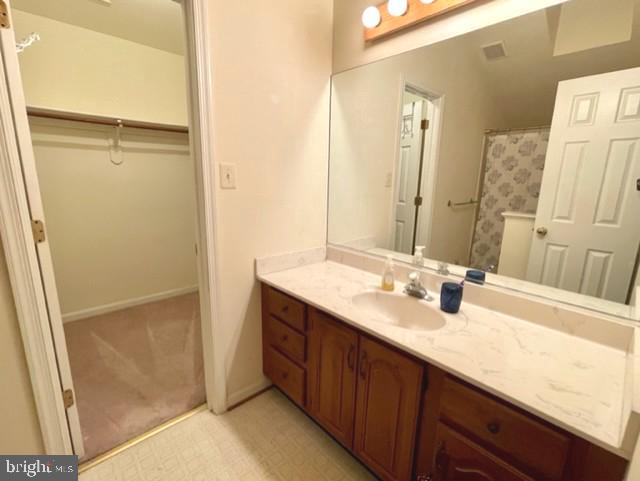 bathroom featuring baseboards, a walk in closet, and vanity