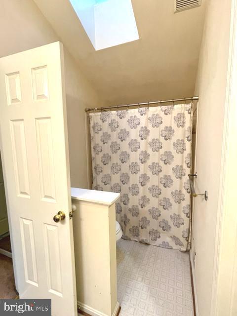 bathroom featuring vaulted ceiling with skylight, visible vents, curtained shower, and tile patterned floors