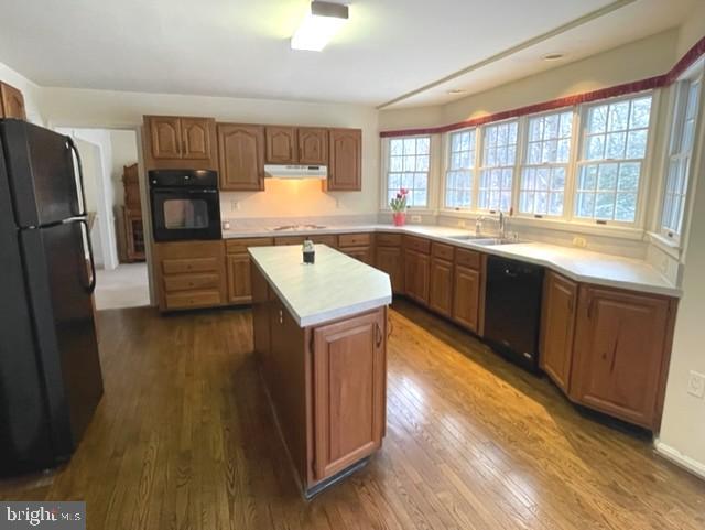 kitchen with under cabinet range hood, dark wood-style flooring, a sink, light countertops, and black appliances