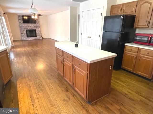 kitchen featuring a kitchen island, wood finished floors, freestanding refrigerator, light countertops, and a fireplace