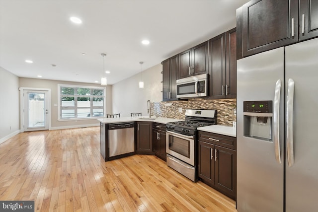 kitchen featuring sink, appliances with stainless steel finishes, kitchen peninsula, pendant lighting, and decorative backsplash