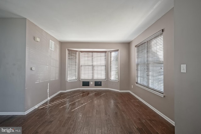 unfurnished room with visible vents, dark wood finished floors, and baseboards