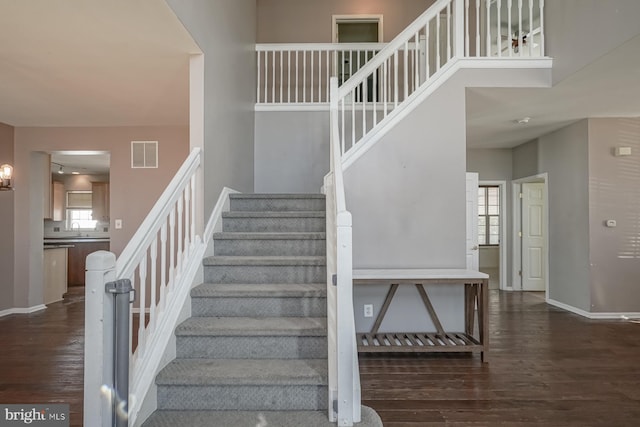 stairway with a towering ceiling, wood finished floors, visible vents, and baseboards