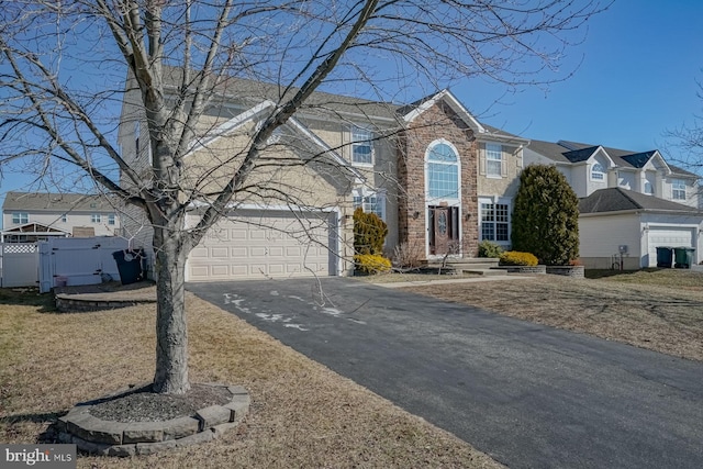 traditional-style house featuring a garage, stone siding, a residential view, and aphalt driveway