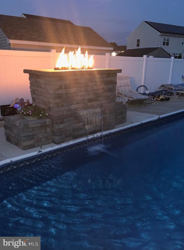 pool at dusk with an outdoor fire pit, fence, and a fenced in pool