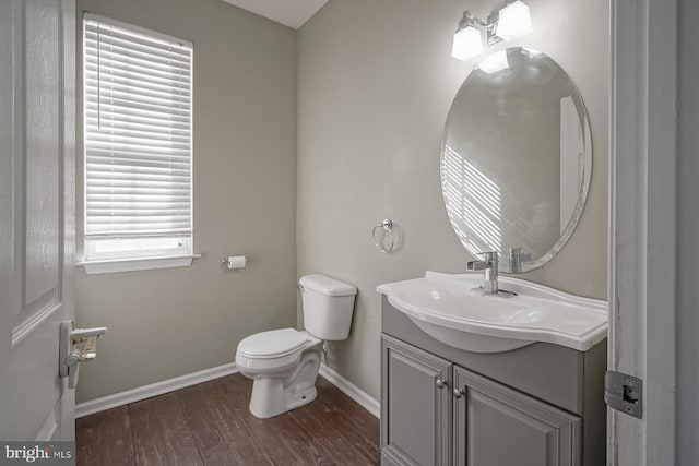 half bathroom with baseboards, vanity, toilet, and wood finished floors