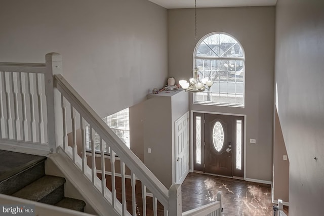 entryway featuring dark wood finished floors, a towering ceiling, a chandelier, baseboards, and stairs