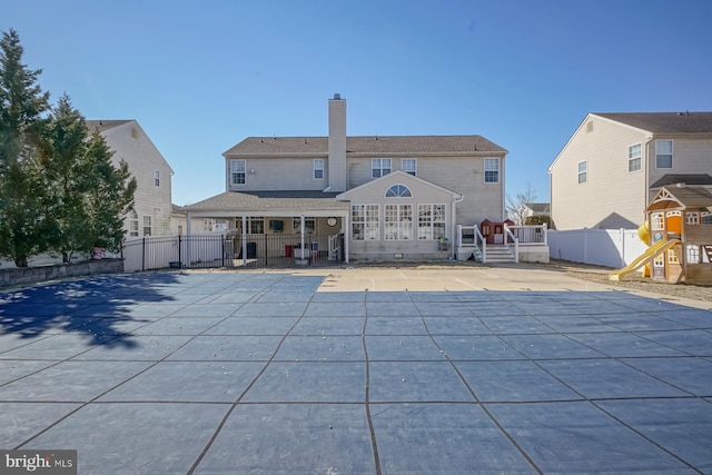 rear view of house with a playground, fence, a fenced in pool, a chimney, and a patio area