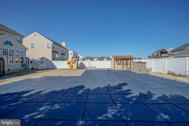 view of swimming pool featuring a fenced backyard, a residential view, an outdoor structure, a patio area, and a shed