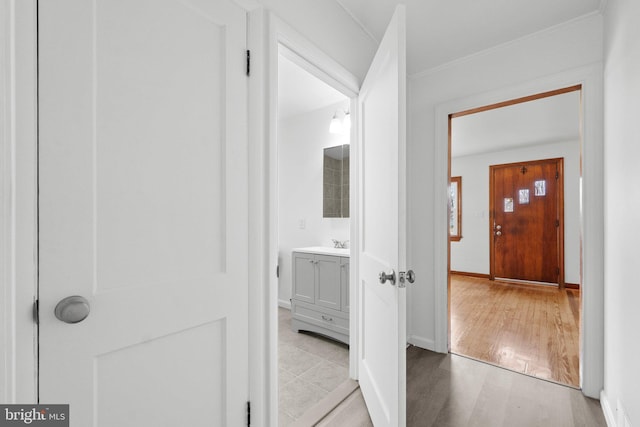 corridor with ornamental molding, sink, and light wood-type flooring