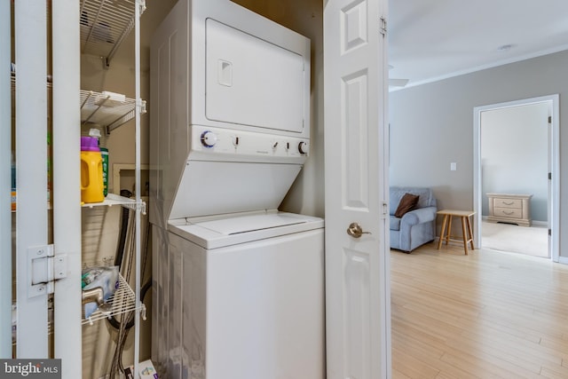 laundry area featuring stacked washer and dryer, crown molding, and light wood-type flooring