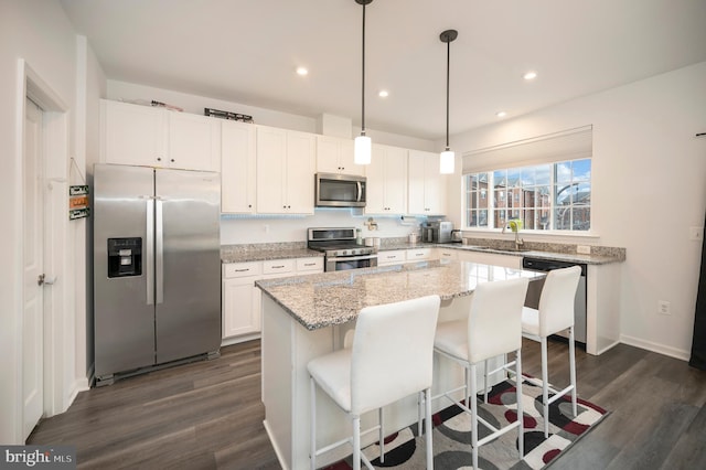 kitchen with decorative light fixtures, a kitchen island, white cabinets, and appliances with stainless steel finishes