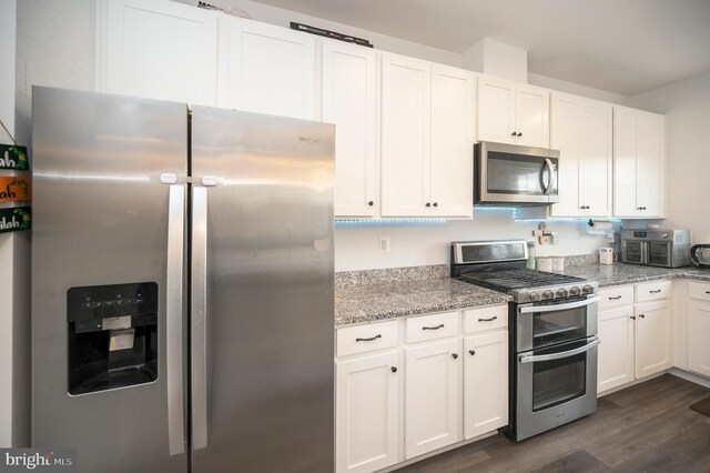 kitchen with dark hardwood / wood-style flooring, appliances with stainless steel finishes, white cabinets, and light stone counters