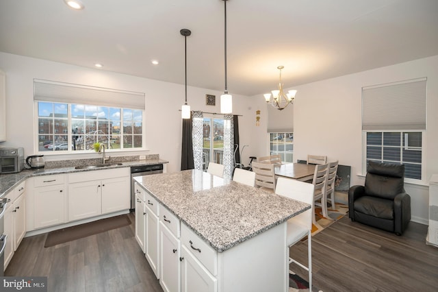 kitchen with white cabinetry, sink, hanging light fixtures, a center island, and light stone counters