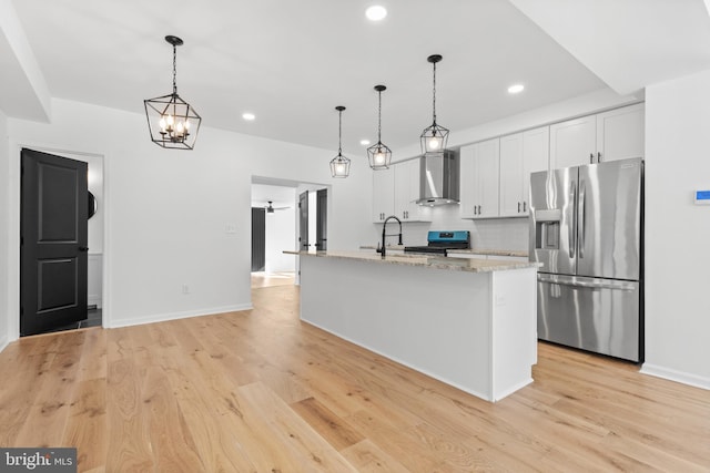 kitchen with white cabinetry, light stone counters, a center island with sink, appliances with stainless steel finishes, and wall chimney range hood