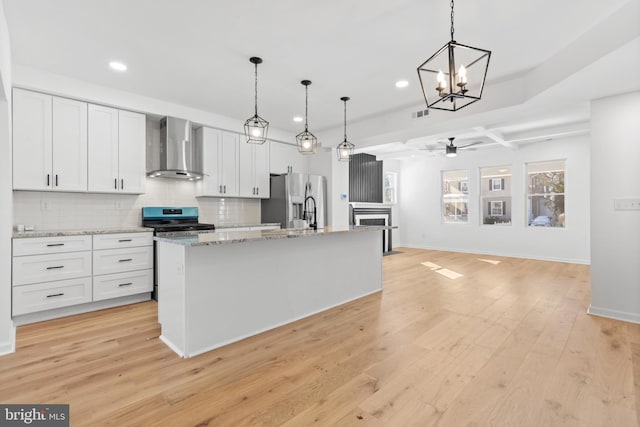 kitchen with decorative light fixtures, white cabinets, wall chimney range hood, stainless steel appliances, and a center island with sink