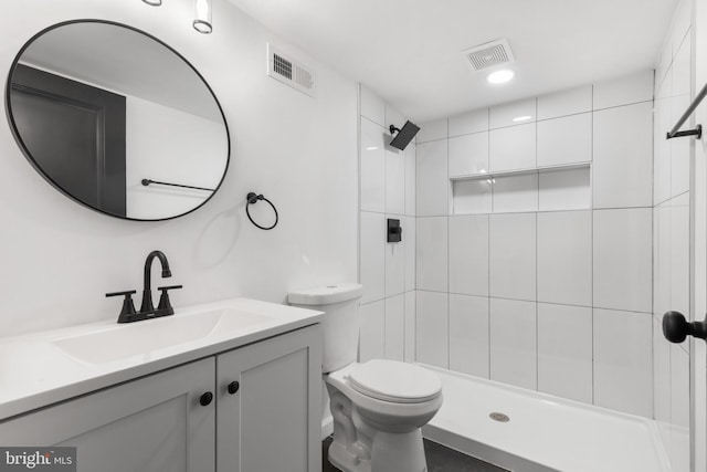 bathroom featuring vanity, a tile shower, and toilet