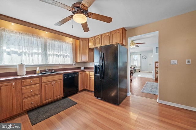 kitchen with dark countertops, a sink, black appliances, light wood-type flooring, and baseboards