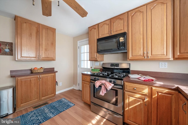 kitchen featuring stainless steel range with gas cooktop, light wood finished floors, visible vents, black microwave, and baseboards