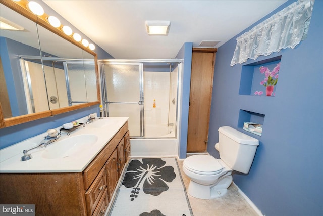 full bathroom featuring double vanity, shower / bath combination with glass door, a sink, and toilet