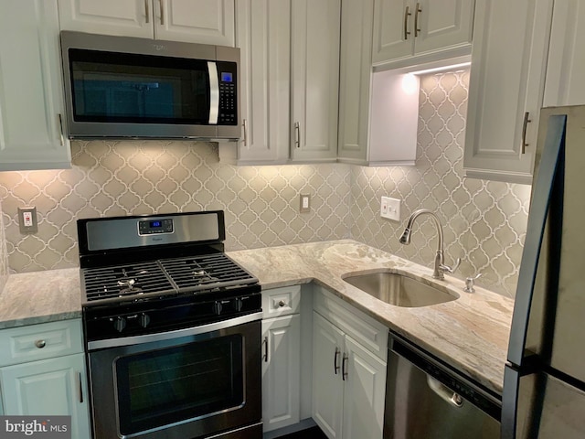 kitchen with sink, white cabinetry, light stone counters, stainless steel appliances, and decorative backsplash