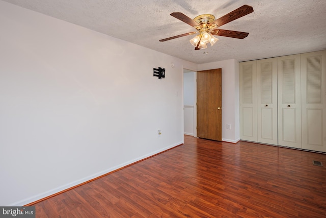 unfurnished bedroom with ceiling fan, dark wood-type flooring, a textured ceiling, and a closet