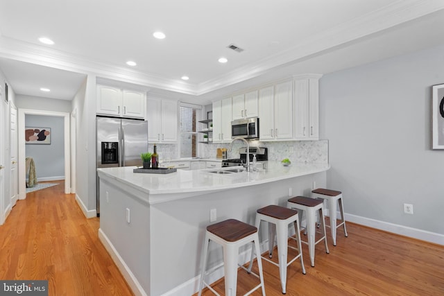 kitchen featuring appliances with stainless steel finishes, kitchen peninsula, white cabinets, decorative backsplash, and a raised ceiling