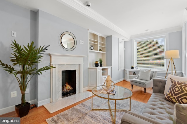 living room featuring ornamental molding, a high end fireplace, light hardwood / wood-style flooring, and built in features