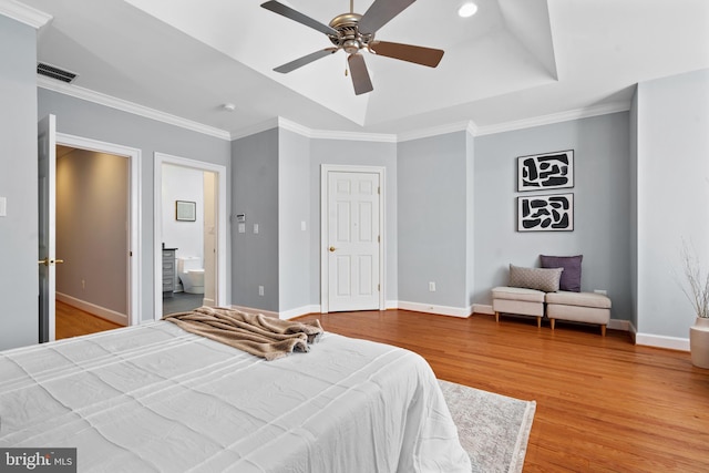 bedroom featuring ensuite bathroom, ornamental molding, a raised ceiling, ceiling fan, and light hardwood / wood-style floors