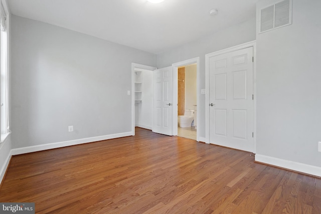 unfurnished bedroom with ensuite bathroom, a spacious closet, hardwood / wood-style floors, and a closet