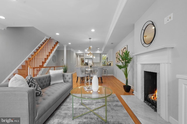 living room with a notable chandelier, ornamental molding, light hardwood / wood-style floors, and a premium fireplace