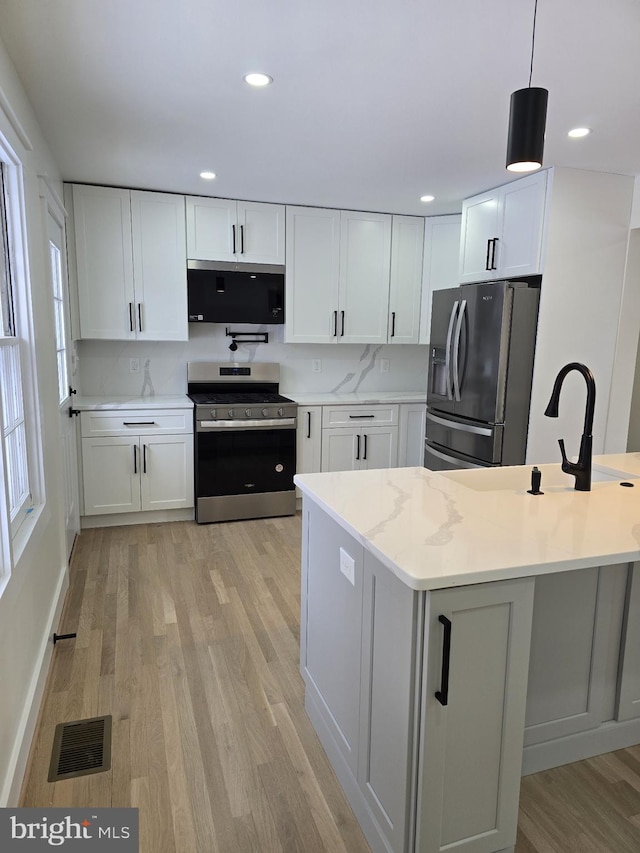 kitchen featuring appliances with stainless steel finishes, white cabinetry, hanging light fixtures, light stone counters, and light hardwood / wood-style floors