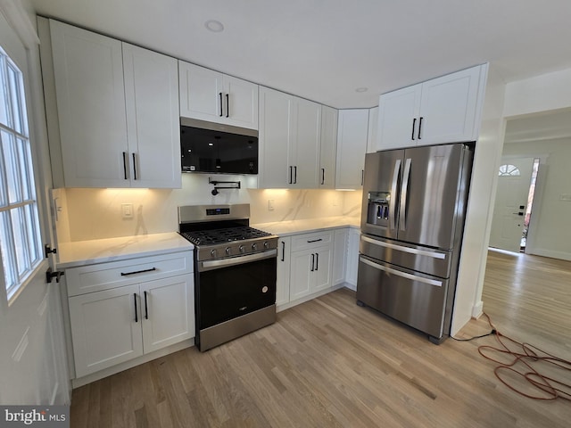 kitchen with stainless steel appliances, white cabinetry, decorative backsplash, and light hardwood / wood-style flooring