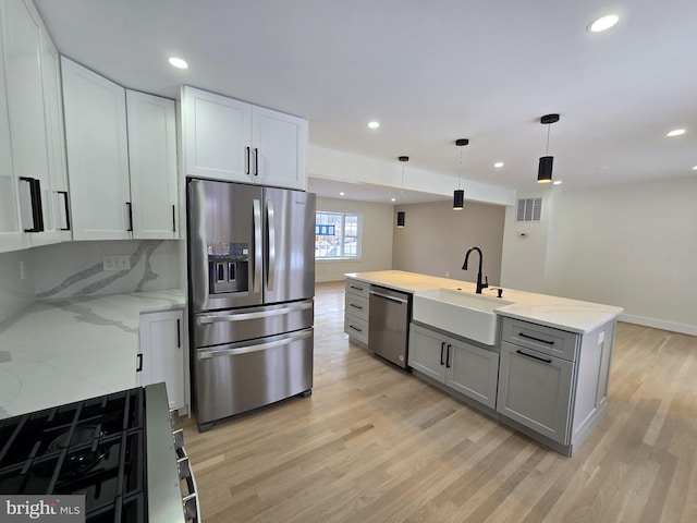 kitchen featuring appliances with stainless steel finishes, sink, white cabinets, hanging light fixtures, and light stone countertops