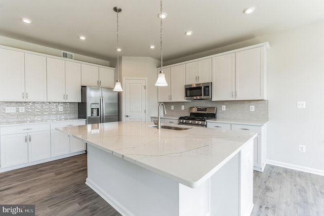 kitchen featuring appliances with stainless steel finishes, white cabinetry, sink, light stone countertops, and a center island with sink