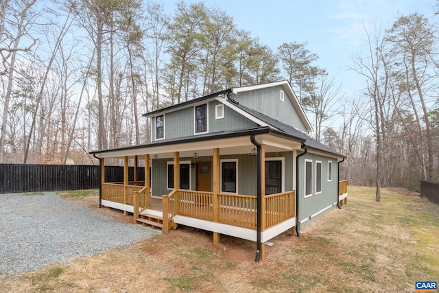 view of front of home with covered porch, a shingled roof, gravel driveway, and fence