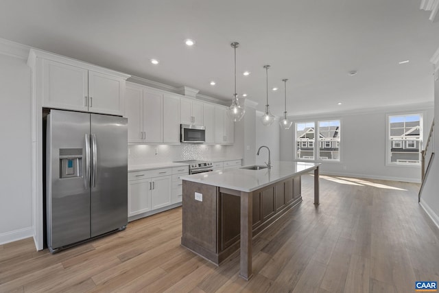 kitchen with appliances with stainless steel finishes, white cabinetry, sink, hanging light fixtures, and a kitchen island with sink