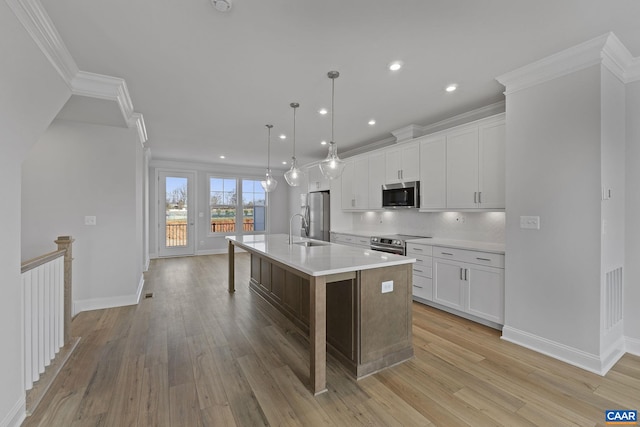 kitchen with decorative light fixtures, stainless steel appliances, an island with sink, and white cabinets