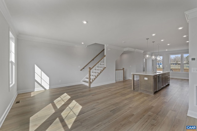 kitchen featuring decorative light fixtures, an island with sink, sink, hardwood / wood-style flooring, and crown molding