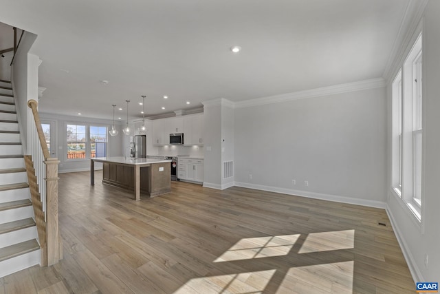 kitchen featuring appliances with stainless steel finishes, sink, white cabinets, hanging light fixtures, and a kitchen island with sink