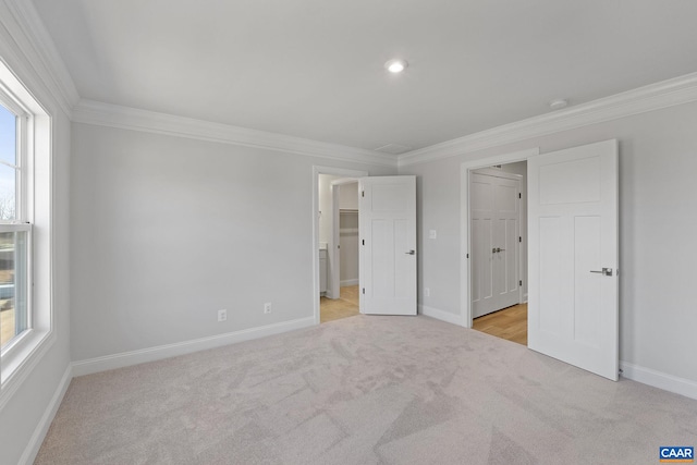 unfurnished bedroom featuring crown molding, a walk in closet, and light colored carpet