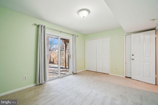 unfurnished bedroom with multiple closets, light colored carpet, and access to outside